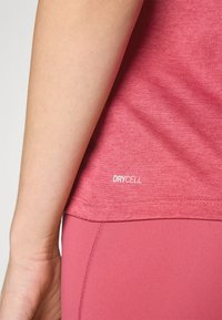 Lyst rosa treningstrøye med korte ermer og en glatt tekstur. Har en "DRYCELL"-label i hvitt nær nederkanten.