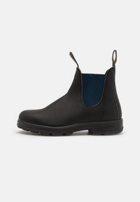 Botín Chelsea de cuero negro con panel lateral elástico azul, lengüeta y suela de goma texturizada para mayor agarre. Acabado liso con punta redondeada.