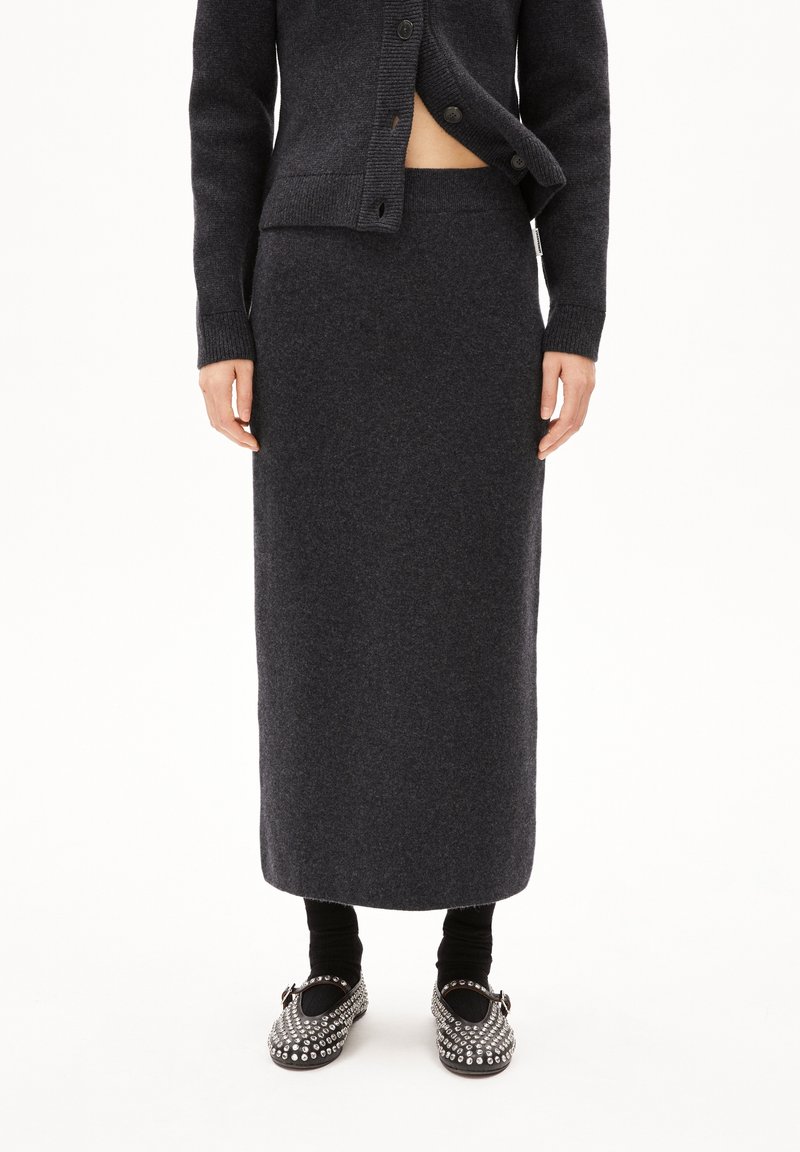 Długa wełniana spódnica w ciemnoszarym kolorze z dopasowanym pasem. Połączona z czarnymi legginsami i butami zdobionymi srebrnymi detalami. Miękka tekstura i gładki design.