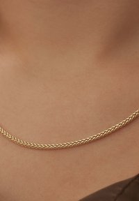 Collier en chaîne en or avec un design tressé, présentant une texture lisse et brillante qui repose élégamment sur la peau.