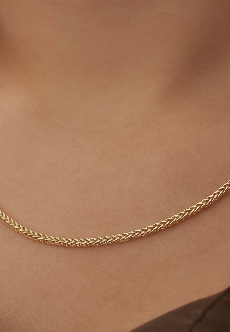Collier en chaîne en or avec un design tressé, présentant une texture lisse et brillante qui repose élégamment sur la peau.