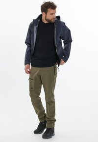 Vattentålig marinblå jacka, svart skjorta, olivgröna cargobyxor med fickor och svarta vandringskängor. Avslappnad utomhusförberedelseoutfit.