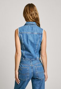 Denimová vesta s golierom, bez rukávov a prispôsobeným strihom. Svetlomodrá farba s viditeľným šitím a vreckami.