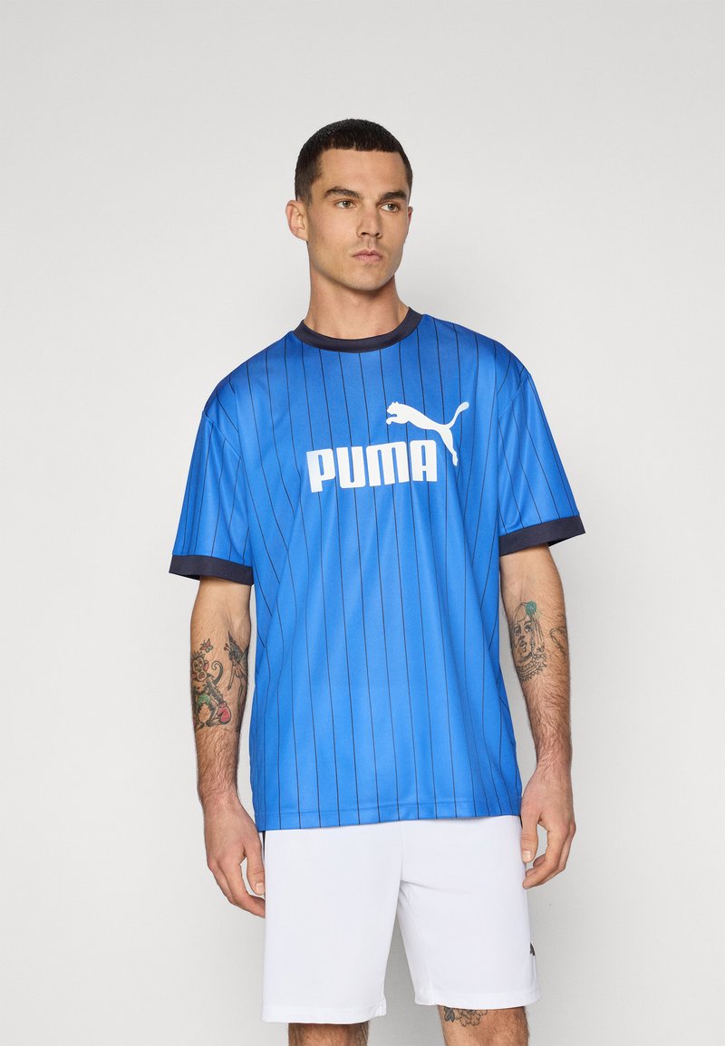 Blå atletisk trøje med lodrette striber, korte ærmer og rund halsudskæring. Har hvidt "PUMA" logo og emblem på brystet.