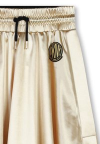 Jupe en satin beige avec une taille élastique, un cordon de serrage noir et un patch rond noir affichant "DKNY NEW YORK CITY" sur le côté.