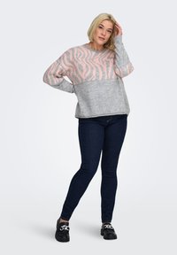 Grijze trui met roze zebraprint, lange mouwen, geribde halslijn en zoom, gecombineerd met donkere jeans en zwarte schoenen. Contrasterende effen kleur en patroon.