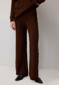 Ruskea kabelineule villapaita ja leveälahkeiset housut, joissa on tekstuuri. Asusteena on teräväkärkiset mustat saappaat.