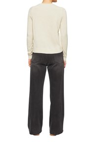 Pull en tricot beige clair à manches longues, associé à un pantalon large gris foncé avec poches arrière et détails de couture visibles.
