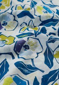 Witte stof met een bloemenpatroon van blauwe, paarse en gele viooltjes en groene bladeren. Zachte textuur, licht gekreukt.