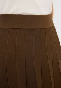 Hnědá plisovaná sukně s širokým, elastickým pasem. Materiál má žebrovanou strukturu, která zobrazuje vertikální linie po celé látce.