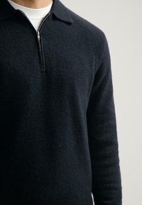 Dunkelblauer Pullover aus weichem, strukturiertem Stoff. Mit Reißverschlusskragen und langen Ärmeln in lässiger Passform.