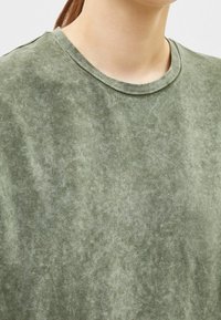 Grön kortärmad T-shirt med rundad halsringning. Tyget har en mjuk, strukturerad, något blekt yta. Inga mönster eller detaljer synliga.