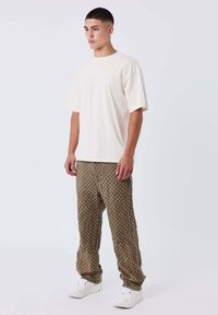 Camiseta corta de manga con un color crema combinada con pantalones marrones de patrón con un diseño floral. Zapatillas blancas completan el conjunto.