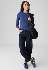 Marineblaues Langarmshirt, dunkelblaue Denim-Hosen mit weitem Bein, blaue Wildlederschuhe und eine schwarze Schultertasche, mit einem lässigen, entspannten Schnitt.