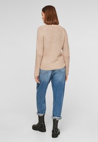 Beige gebreide trui met een gestructureerde afwerking, gecombineerd met blauw jeans met opgerolde manchetten en zwarte enkellaarsjes. Het ontwerp heeft een eenvoudige, getailleerde silhouwet.