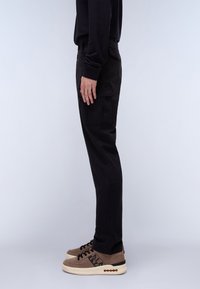 Black cargo pants with side pockets, straight-leg design, and elastic waistband, paired with brown sneakers showcasing laces and a logo.