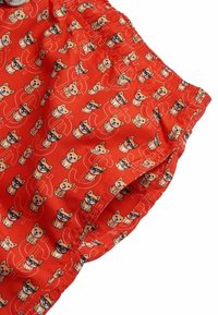 Pantaloni corti rossi in tessuto con un motivo ripetuto di cani dei cartoni animati in varie pose, con accenti neri e arancioni. Vita elastica in cima.