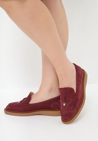 Bordeaux fløjlsloafers med en beige gummisål, der har en dekorativ sløjfe og metalaccent, med et lavprofileret design.