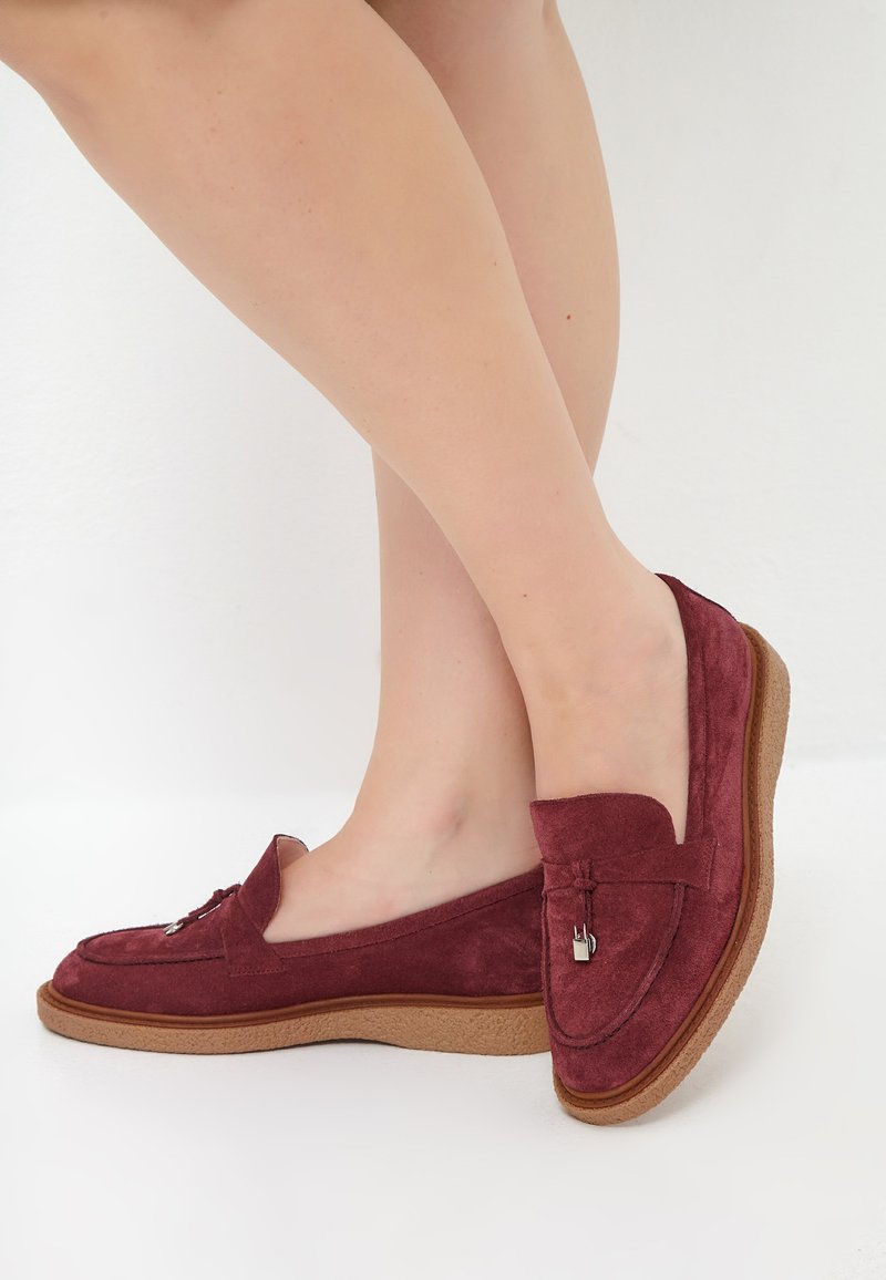 Bordeaux fløjlsloafers med en beige gummisål, der har en dekorativ sløjfe og metalaccent, med et lavprofileret design.
