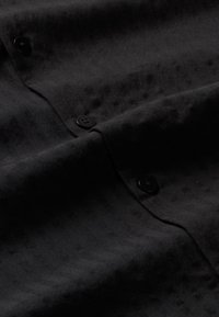 Schwarzes Stoffhemd mit Knopfleiste und strukturiertem Fischgrätmuster, mit schwarzen Knöpfen und einer weichen, glatten Textur.