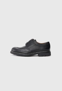 Schwarzer Lederschuh mit abgerundeter Zehenform, Schnürdesign und strukturiertem Obermaterial. Besonders auffällig ist der kontrastierende weiße Stich entlang der Sohle.