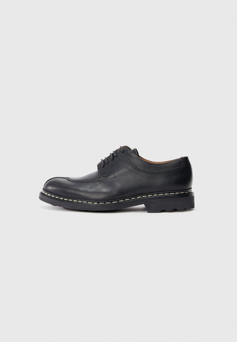 Schwarzer Lederschuh mit abgerundeter Zehenform, Schnürdesign und strukturiertem Obermaterial. Besonders auffällig ist der kontrastierende weiße Stich entlang der Sohle.