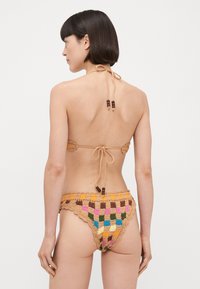 Háčkovaná bikiny v béžovej farbe s viacfarebnými geometrickými vzormi. Obsahujú viazanie za krkom a drevené korálky na popruhoch a páse.