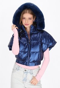 Marinblå vadderad jacka med huva av fuskpäls, glansig yta, kort modell och dragkedja fram, bärs över en ljusrosa långärmad topp.