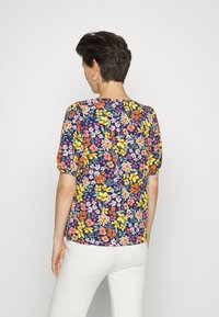 Top com estampa floral em azul marinho, com mangas curtas e bufantes, apresentando flores amarelas, rosas e verdes, combinado com calças brancas texturizadas.