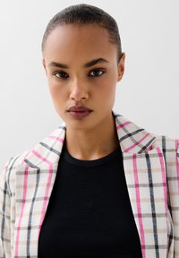 Geruite blazer in crème, roze en grijze tinten, met een gestructureerd design. Zwarte geribbelde tanktop eronder. Glad stoftextuur.