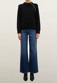 Svart stickad tröja med hög hals och sidoförslutning med dragkedja. Matchas med vida blå jeans och svarta spetsiga ankelboots.