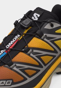 Close-up of yellow and black Salomon trail running shoe with quick-pull lacing system and visible brand logo on tongue and side.