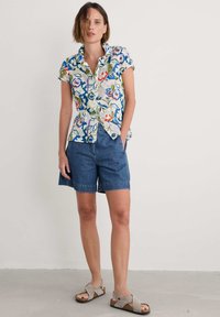 Floral short-sleeve button-up shirt with green, blue, and red designs; denim shorts; gray cross-strap sandals; light background.