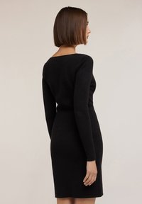 Vestido negro ajustado con mangas largas, escote barco y una textura de punto suave, que exhibe un diseño minimalista con una longitud a mitad del muslo.