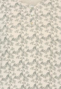 Napapaita, jossa on vaalean beige tausta ja herkkä vihreä kukkakuosi. Kaula-aukossa on kolme pientä nappia, jotka lisäävät yksityiskohtia.