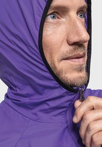 Leichte lila Jacke mit durchgehendem Reißverschluss und Kapuze. Glatte Textur mit schwarzem Rand um die Kapuze und den Reißverschluss.