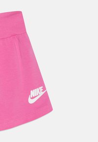 Rozā kokvilnas svārki ar elastīgu jostu, ar baltu Nike logo drukātu apakšējā kreisajā stūrī. Gluda tekstūra, ikdienišķs dizains.