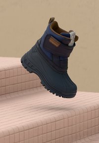 Botte marine imperméable avec une surface texturée, présentant un accent marron au niveau du col et une sangle Velcro pour un maintien sécurisé.