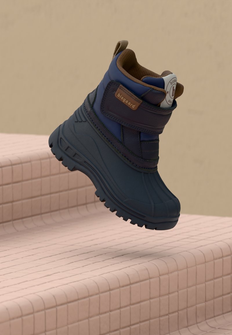 Bota impermeable de color marino con una superficie texturizada, que presenta un acento marrón en el collar y una tira de velcro para un cierre seguro.