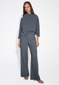 Graue weite Hosen in Kombination mit einem passenden, locker sitzenden Oberteil. Beide Kleidungsstücke haben eine glatte Textur und ein minimalistisches Design.