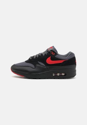 Czarne i ciemnoszare niskie sneakersy z czerwonym logo Nike i podeszwą z poduszką powietrzną, pokazane z boku na jednolitym jasnym tle.