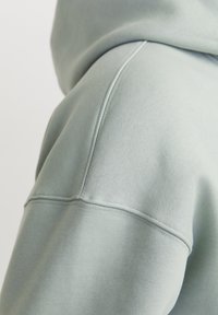 Felpa verde chiaro con tessuto texturizzato, cuciture visibili e vestibilità rilassata. Il tessuto sembra morbido e confortevole.