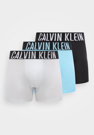 Három férfi boxeralsó fehér, világoskék és fekete színekben, fekete derékpánttal, amelyen vastag fehér betűkkel szerepel a "Calvin Klein" felirat.