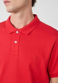 Rood katoenen poloshirt met een kraag, twee knopen aan de voorkant en een textuuraccent van het logo op de linkerborst.