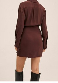 Maroon napit kanavan mekko, joka on valmistettu pehmeästä kankaasta. Siinä on pitkät hihat, kaulus ja kireä vyötärö. Mekko päättyy ylle polvien ja siinä on sivuaukot.