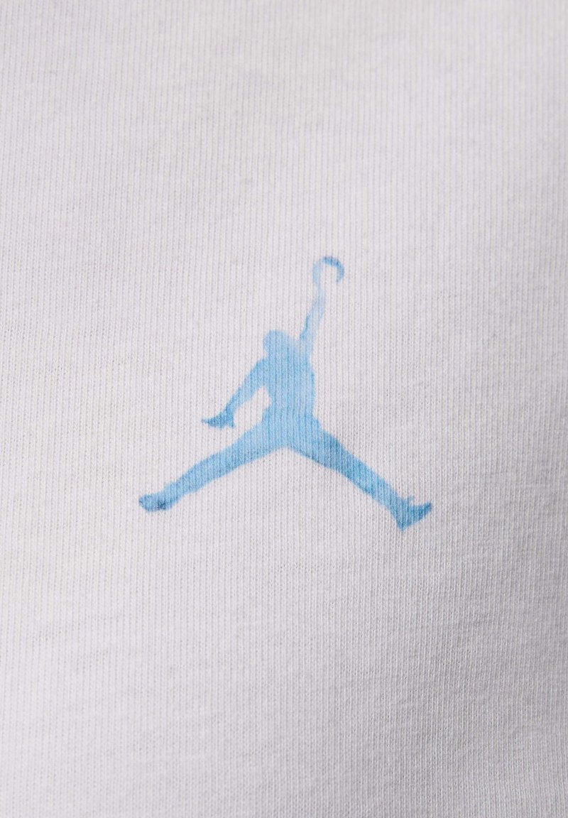 Tela blanca con una textura acanalada presenta un logotipo azul de Jumpman, que representa una figura en silueta en una posición de salto, sosteniendo un baloncesto.