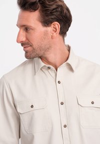 Lichtbeige shirt van katoen, met een gespreide kraag, twee borstzakken en bruine metalen knoopaccenten. Gladde textuur en casual pasvorm.