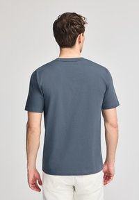 Kortärmad t-shirt i mörkgrå bomull. Klassisk rundhalsad design med slät textur. Har en rak fåll och minimala sömnadsdetaljer.