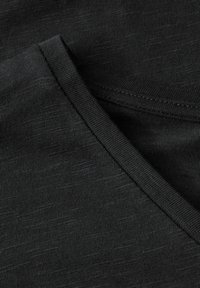 Černá tkanina s jemnou texturou, s kulatým výstřihem a čistým šitím. Materiál vypadá měkký a pružný.