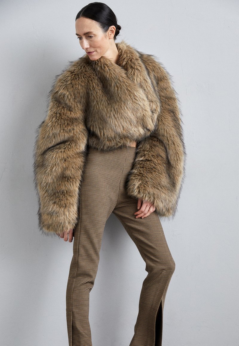 Faux fur cropped jacket in brown with wide sleeves. Paired with brown checkered trousers featuring flared hems and a fitted waistband.